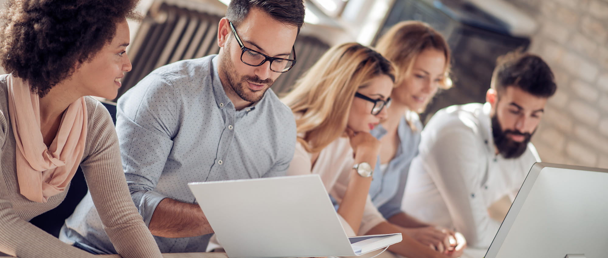 Egy csoport kolléga együtt dolgozik egy asztalnál laptopokkal és dokumentumokkal.