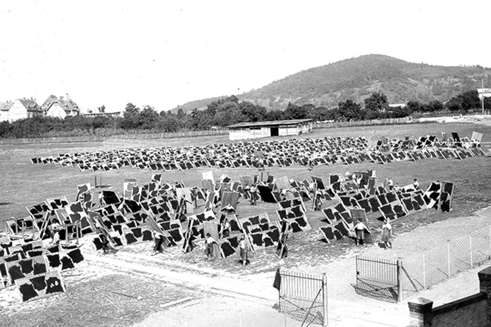 Historical picture of men and women stretching fabrics on wooden boards in a meadow