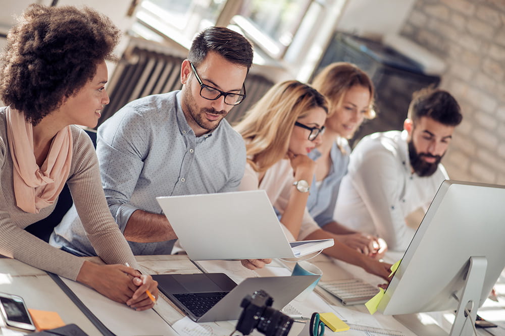 A group of colleagues collaborating at a desk with laptops and documents.