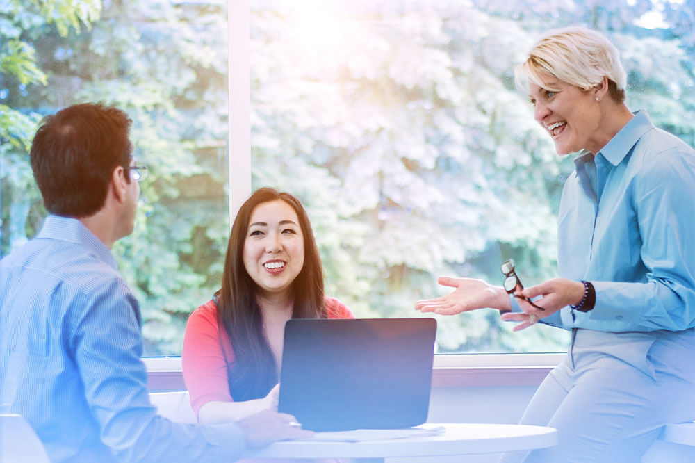 Woman sits in front of laptop and around her are two colleagues