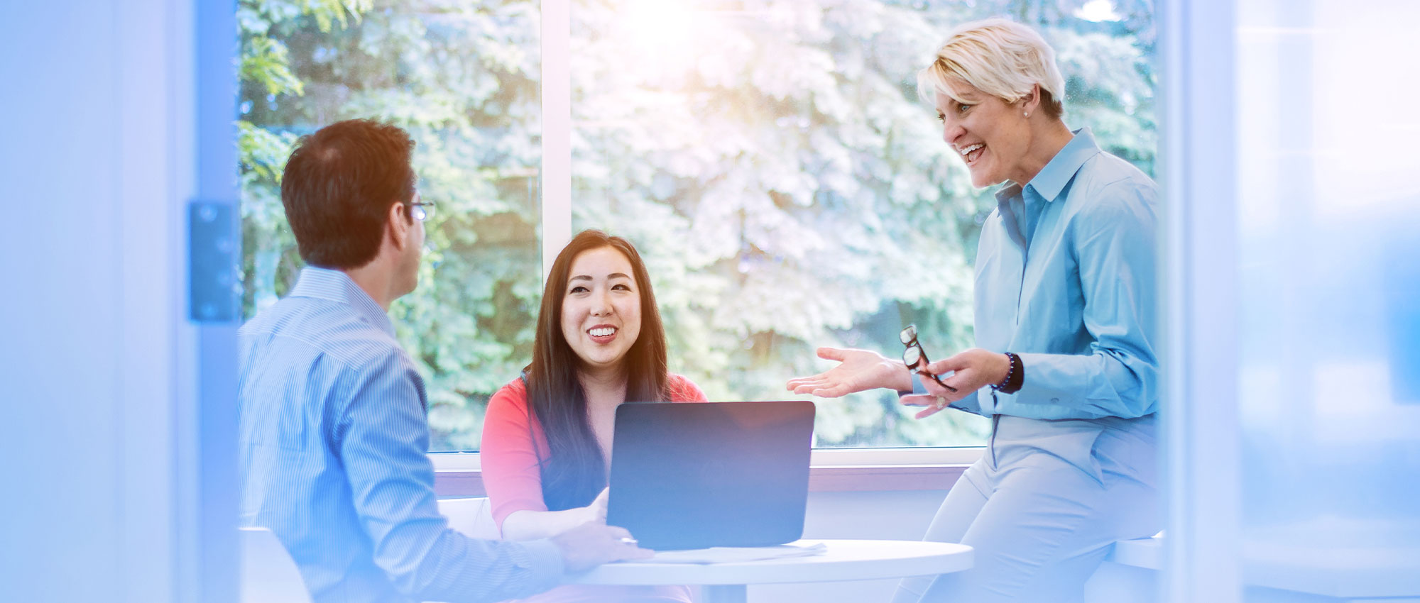 Woman sits in front of laptop and around her are two colleagues