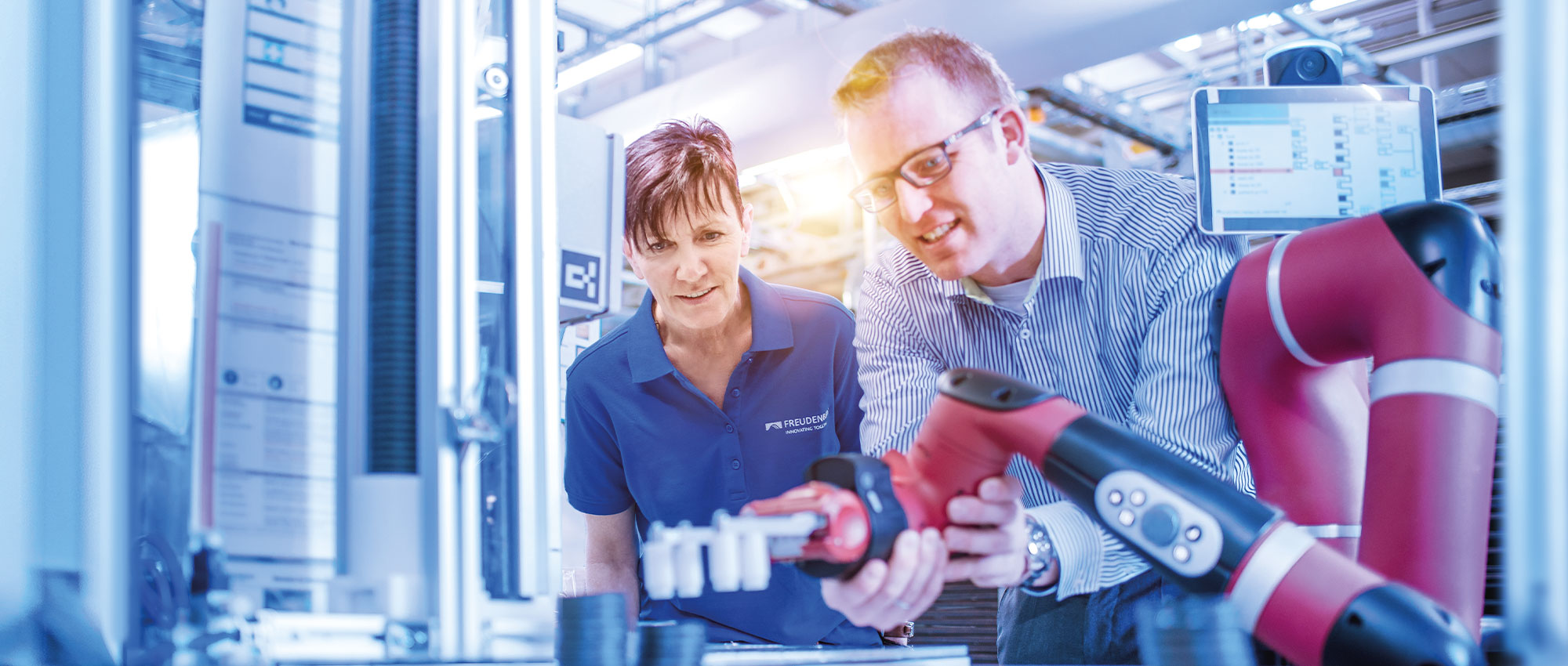 Two employees use a robotic arm in the workshop