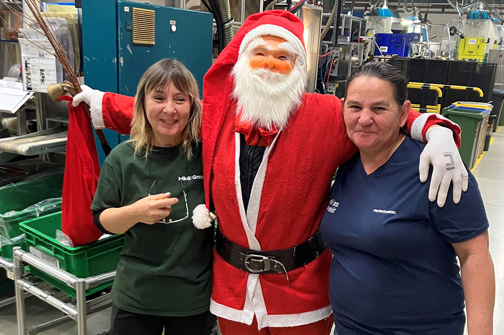 Santa Claus with two employees in his arms in the workshop