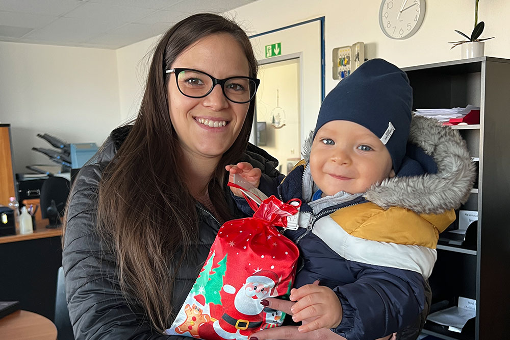 Employee has her son in her arms and holds a Christmas gift