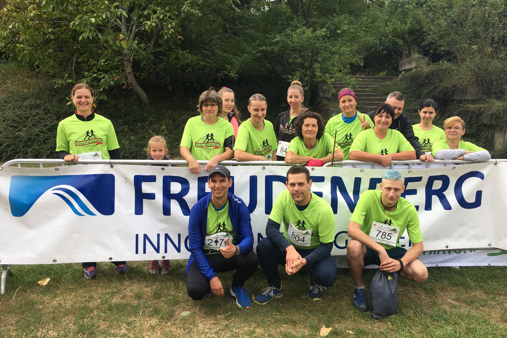 Employees stand behind the Freudenberg banner and a handful of employees squat in front of the banner in sporting competition