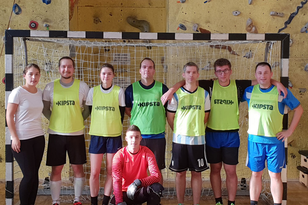 Employees stand in front of goal at indoor soccer event and goalkeeper kneels in front of his team