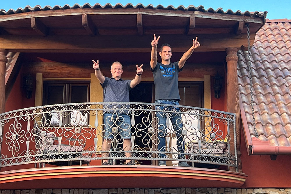 Two employees stand on a balcony and show the peace sign with both hands