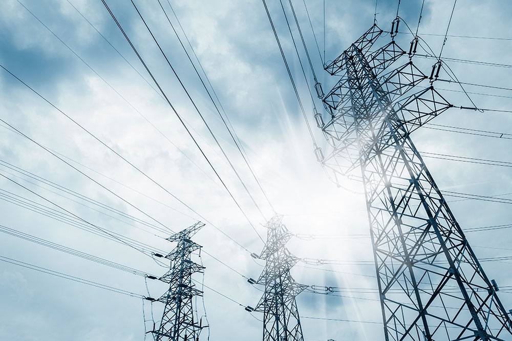 Power transmission tower under blue sky with clouds and piercing sun rays